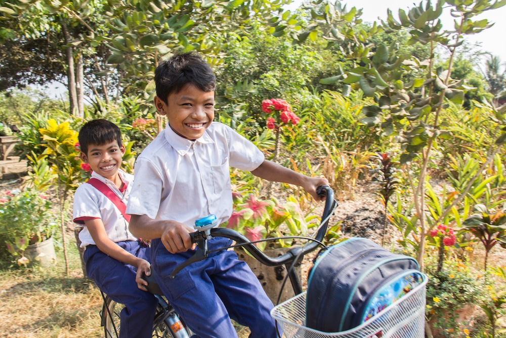 2 smiling Cambodian boys on their way to school on their bicycle