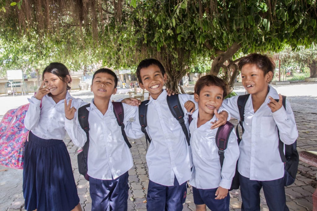 5 smiling Cambodian school children pose for a photograph in their school uniforms and backpacks