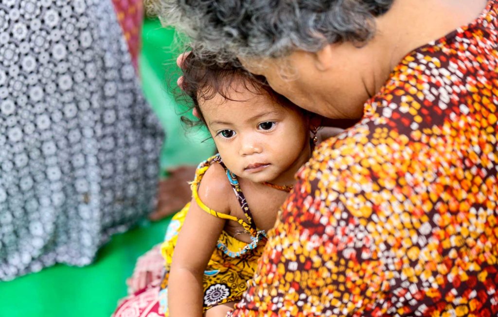 A young Cambodian girl is cradled in the arms of her Grandmother